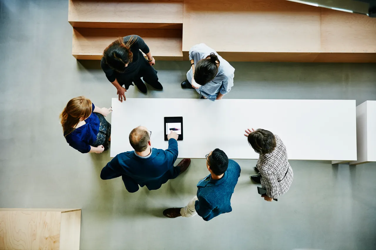 
A diverse group of professionals collaborates around a tablet during a meeting in a modern workspace.